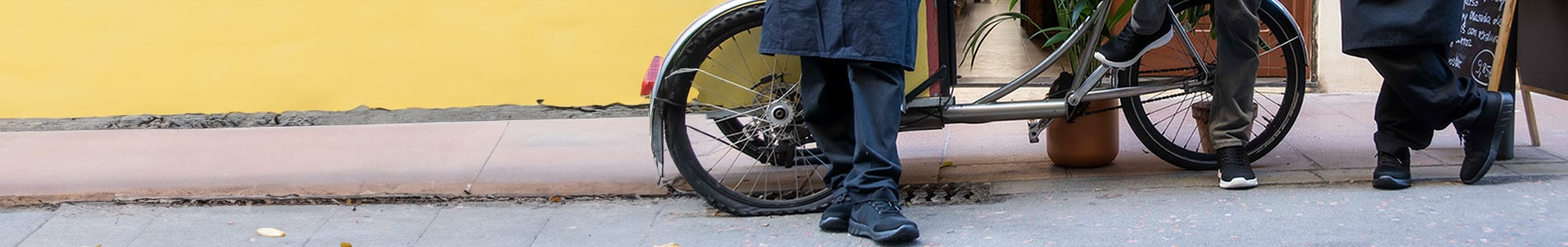 Drie personen dragen zwarte Suecos werkschoenen met demping terwijl ze naast een fiets op een trottoir staan. De comfortabele schoenen zijn geschikt voor langdurig staan en wandelen.